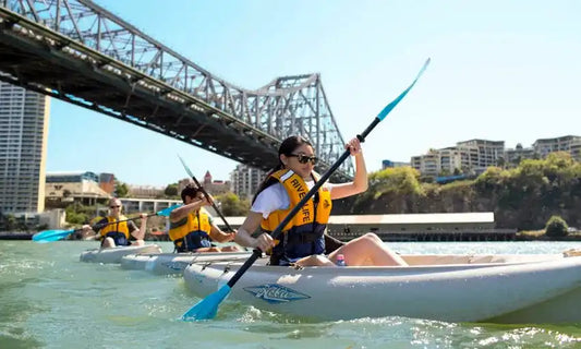 People kayaking on a river with a bridge in the background